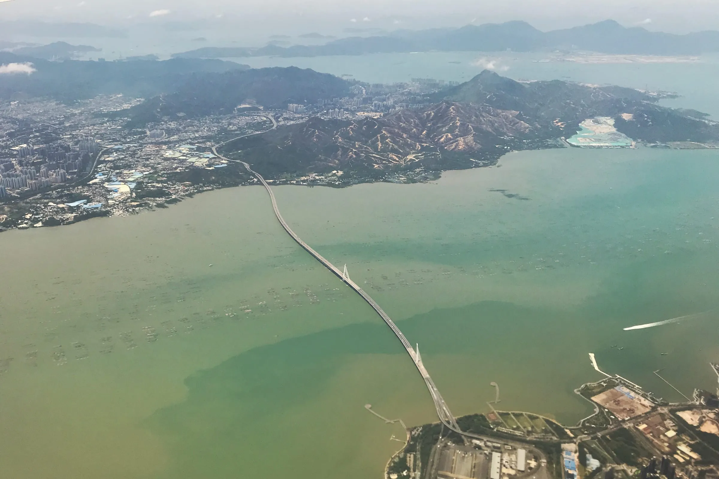 The Shenzhen Bay Bridge running across green water toward the hills of Hong Kong, seen from the air