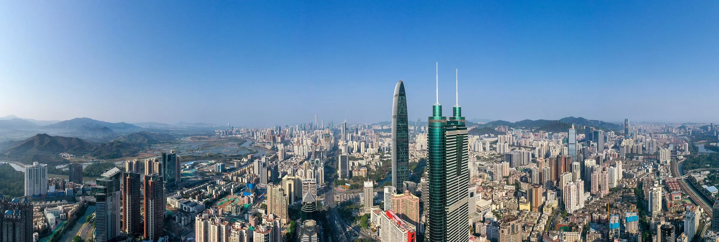A wide view over Shenzhen: dense towers along Shennan Road, low hills behind them under a clear sky